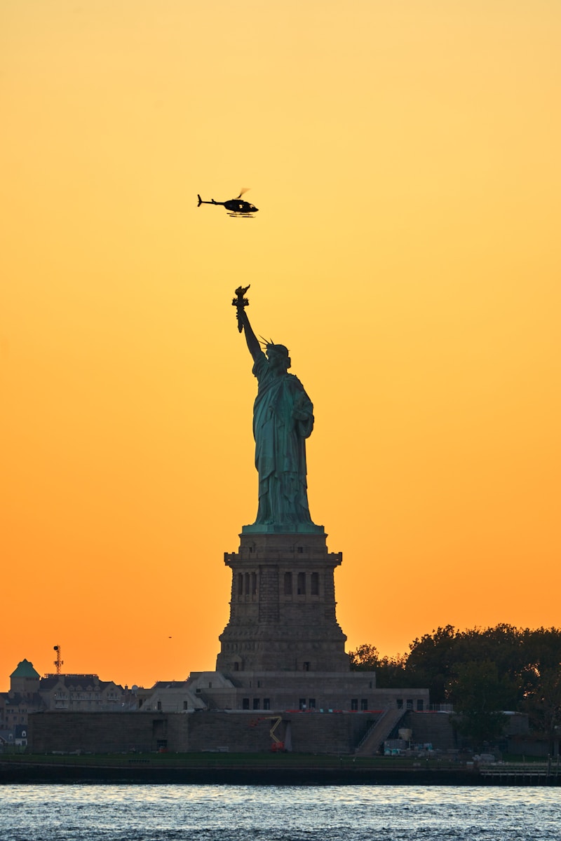 a plane flying over the statue of liberty at sunset