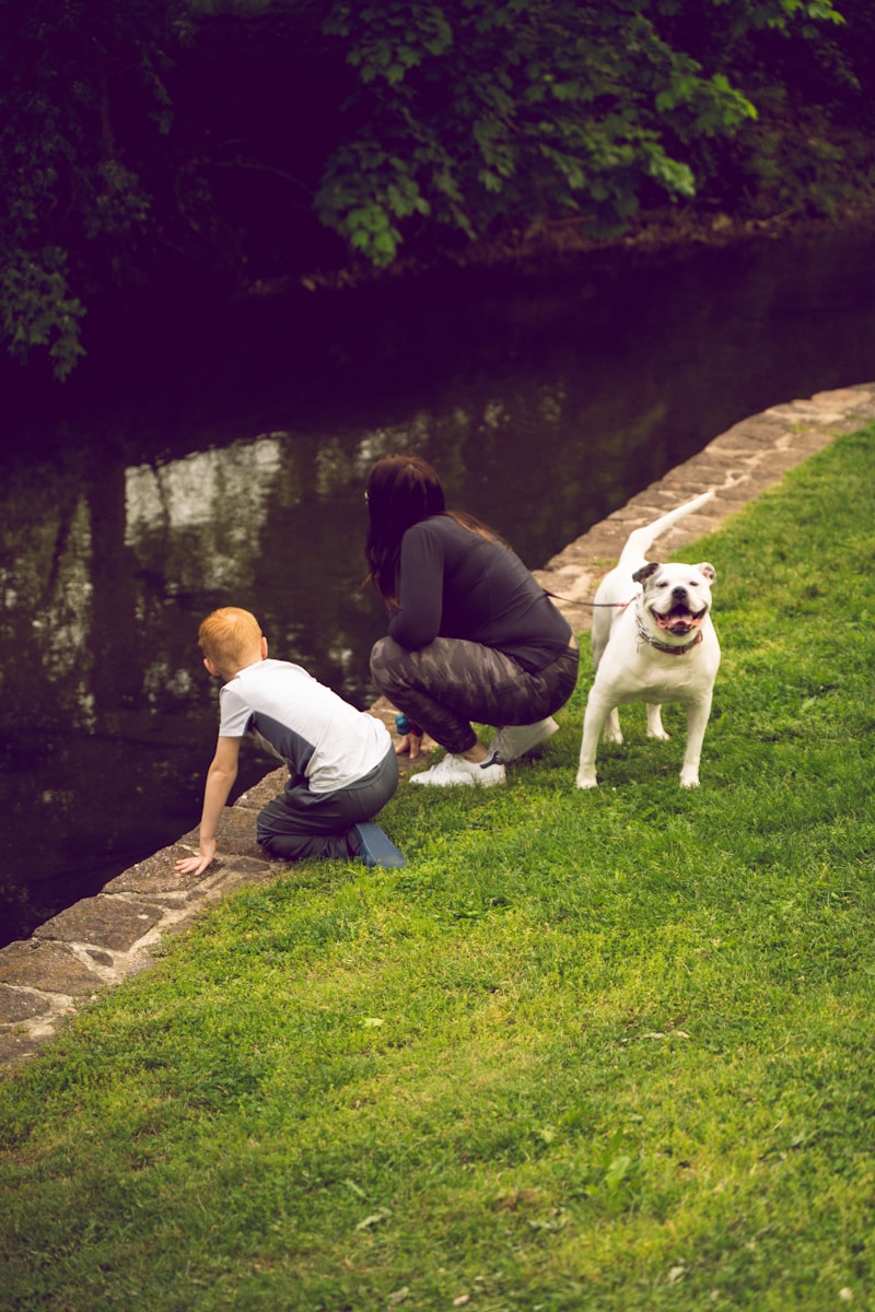 man and woman sitting on green grass field beside white dog during daytime