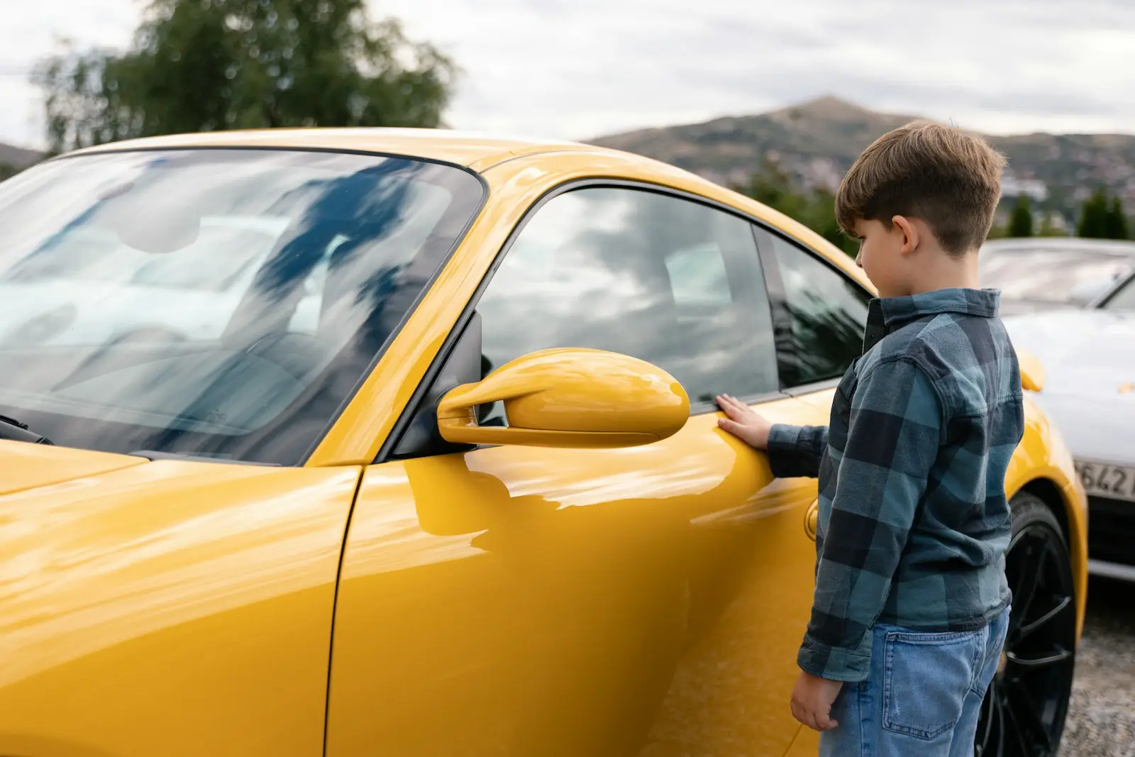 A young boy touches a yellow sports car insured by safeco car insurance