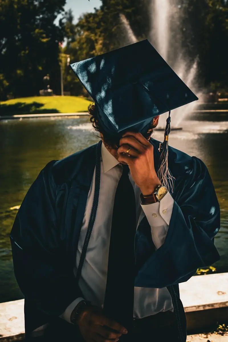 a man in a graduation cap and gown covers his face with his hands